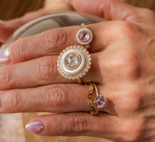Close-up of a hand wearing two gold rings with gemstones on a blurred background