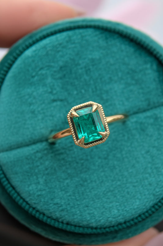 Gold ring with a green gemstone on a teal cushion