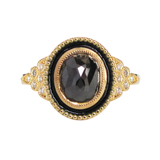 An 18K yellow gold engagement ring with a black diamond centerpiece and smaller clear diamond accents, featuring vitreous glass enamel inlay and miligrain accents.