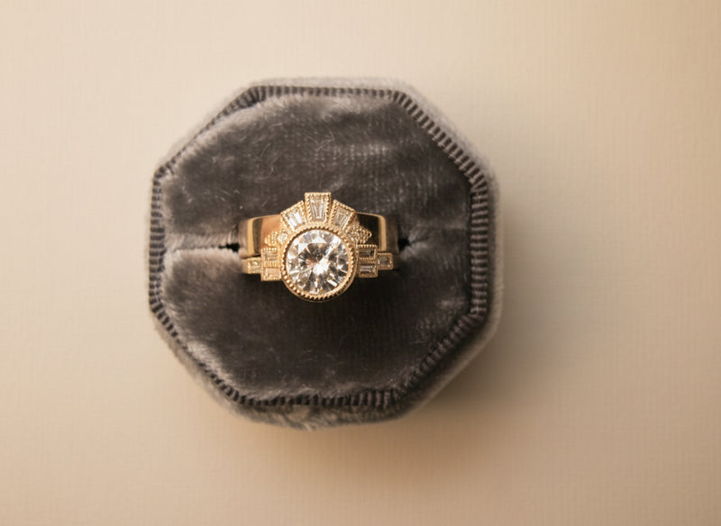 Gold ring with a large diamond in a gray velvet box on a light gray background