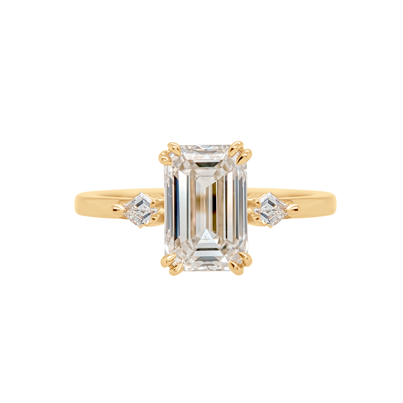 Gold ring with emerald-cut diamond and smaller side stones on a white background
