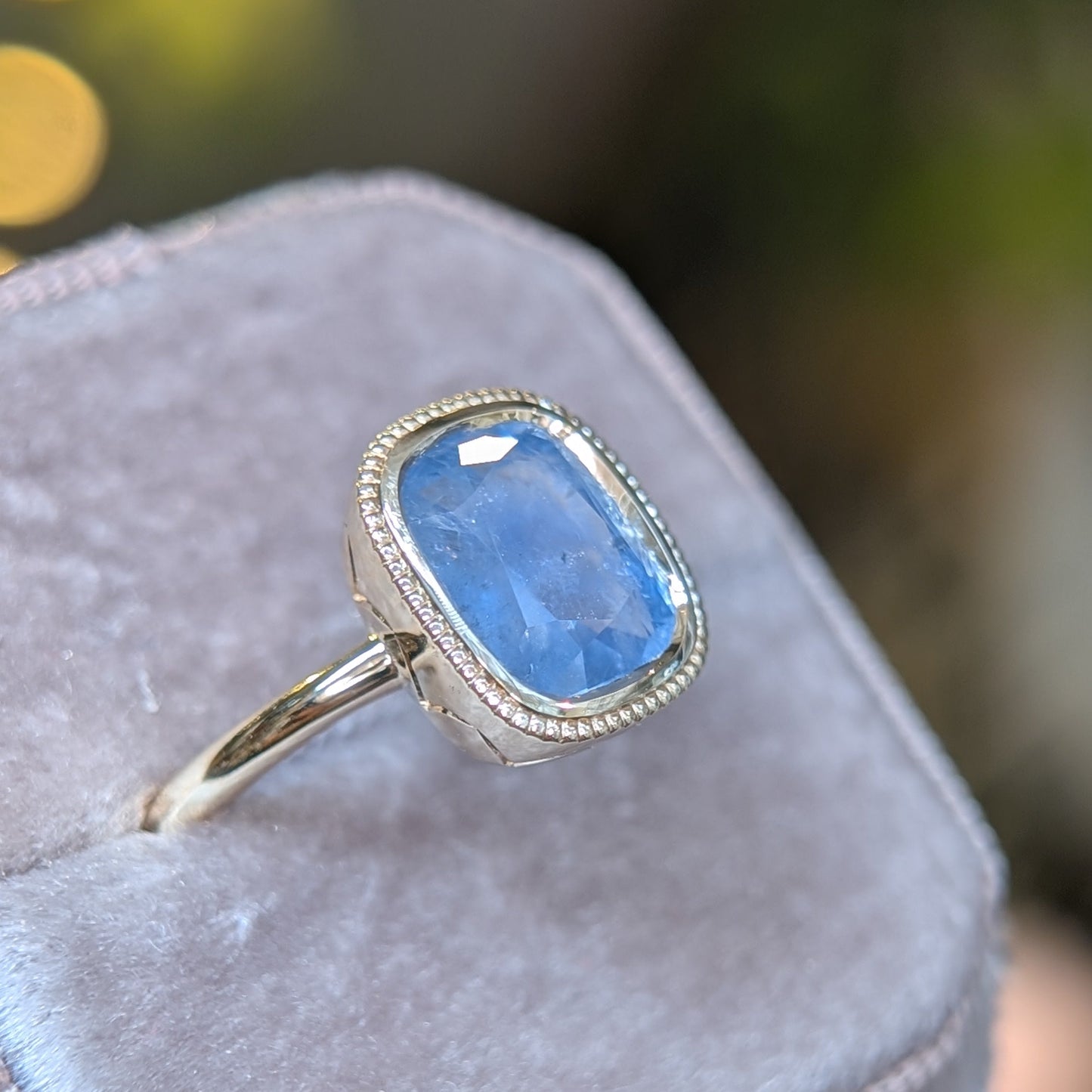 Ring with a blue gemstone on a soft pink cushion