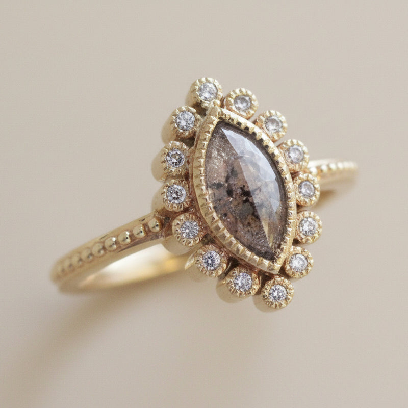 Gold ring with a central stone and diamond accents on a textured beige background