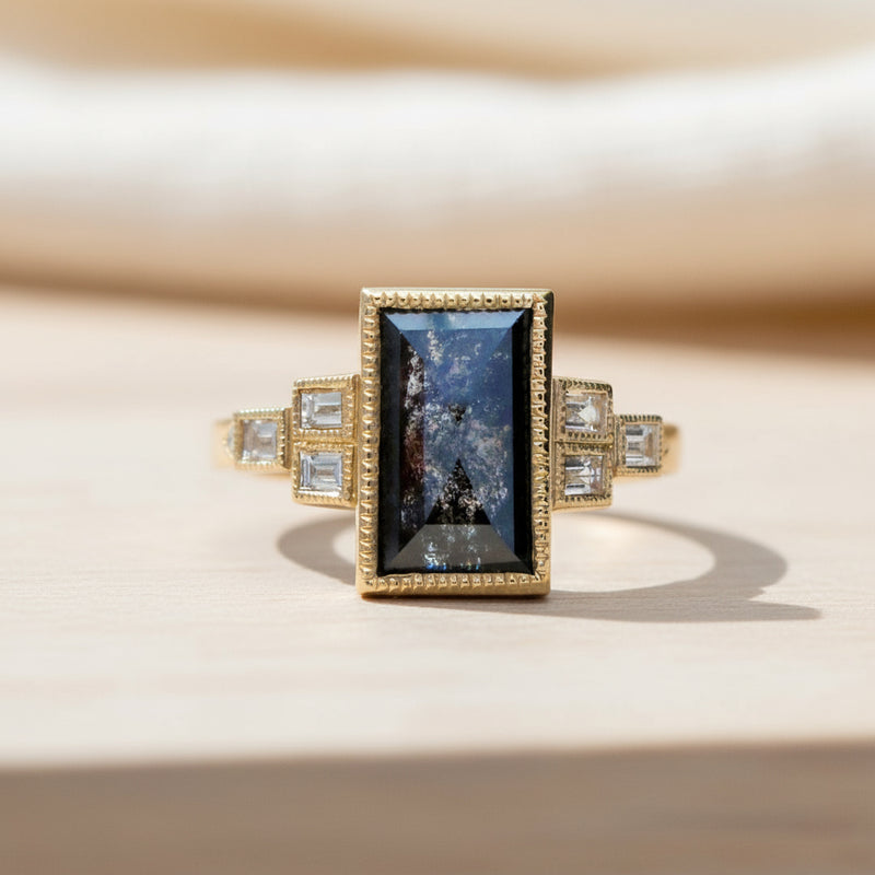 Gold ring with a central black gemstone and smaller diamonds on a white background
