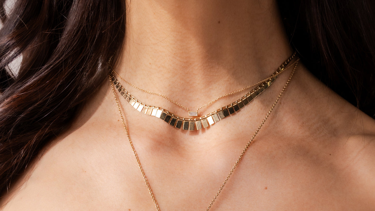 Close-up of a person wearing two gold necklaces with a pink top.