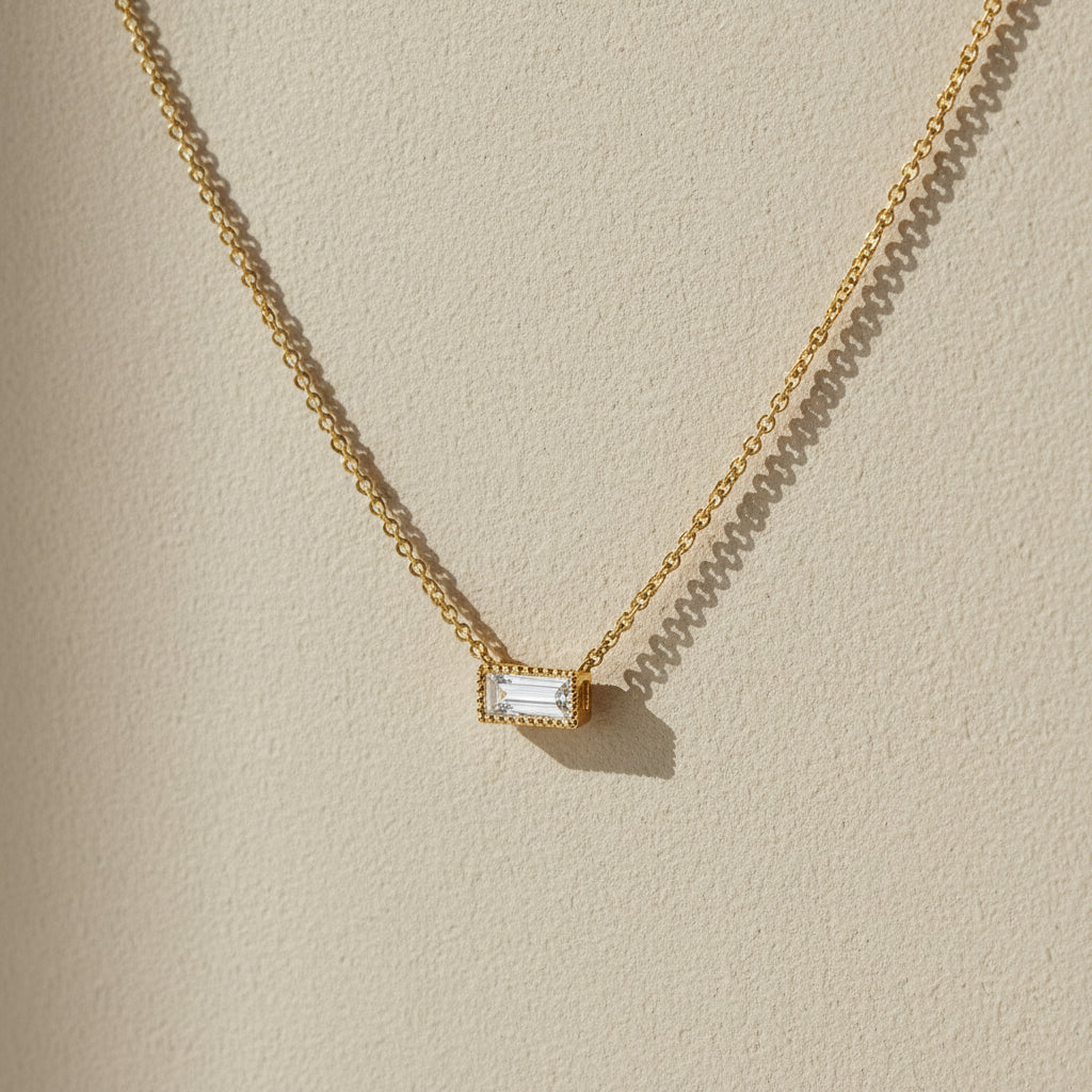 Gold necklace with a rectangular diamond pendant on a white background