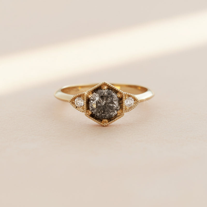 Gold ring with a central dark stone and smaller diamonds on a white background