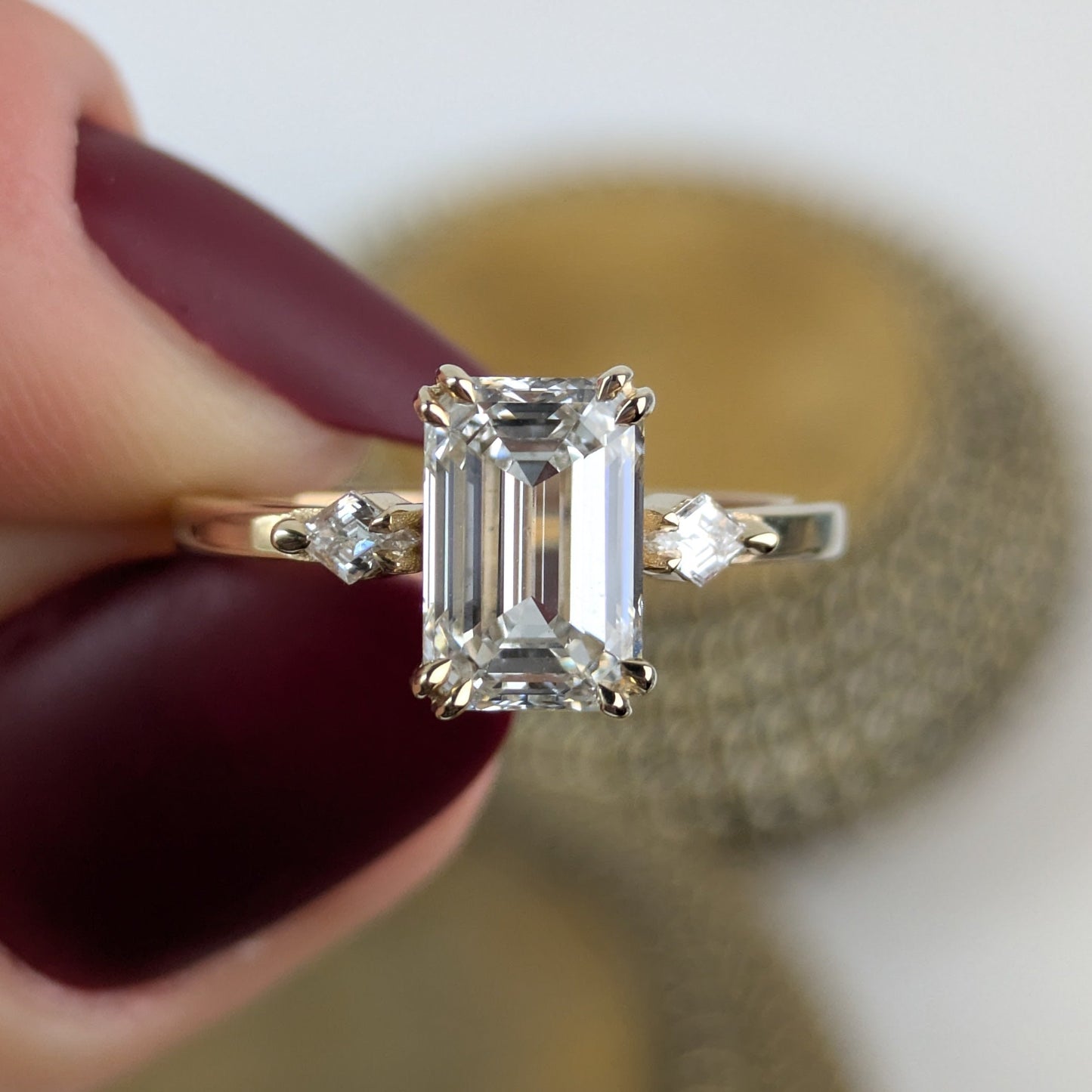 Diamond ring held by a hand with red nail polish on a blurred background