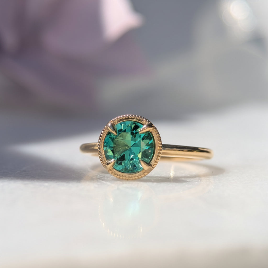Gold ring with a green beryl gemstone on a white surface with a blurred background