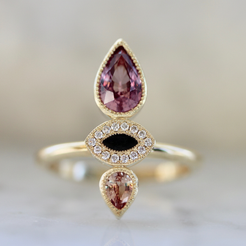 Gold ring with teardrop-shaped gemstones on a blurred background
