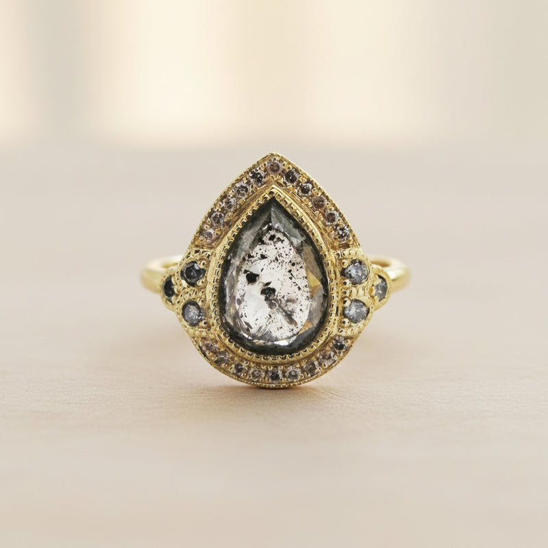 Gold ring with a teardrop-shaped central stone and smaller stones on a white background