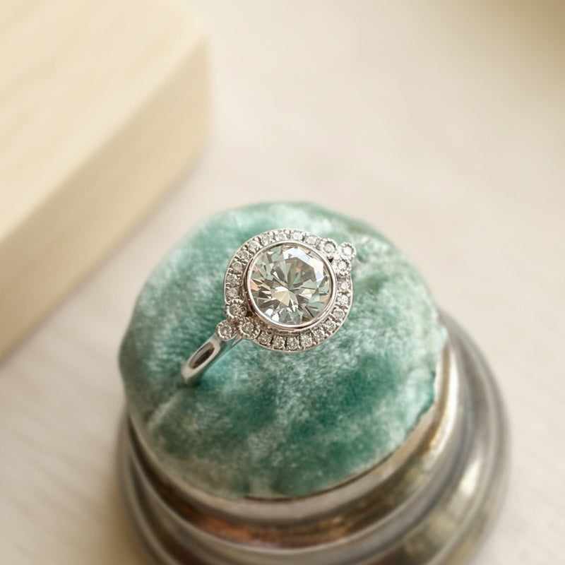 Silver ring with a large central gemstone on a green cushion inside a silver box.