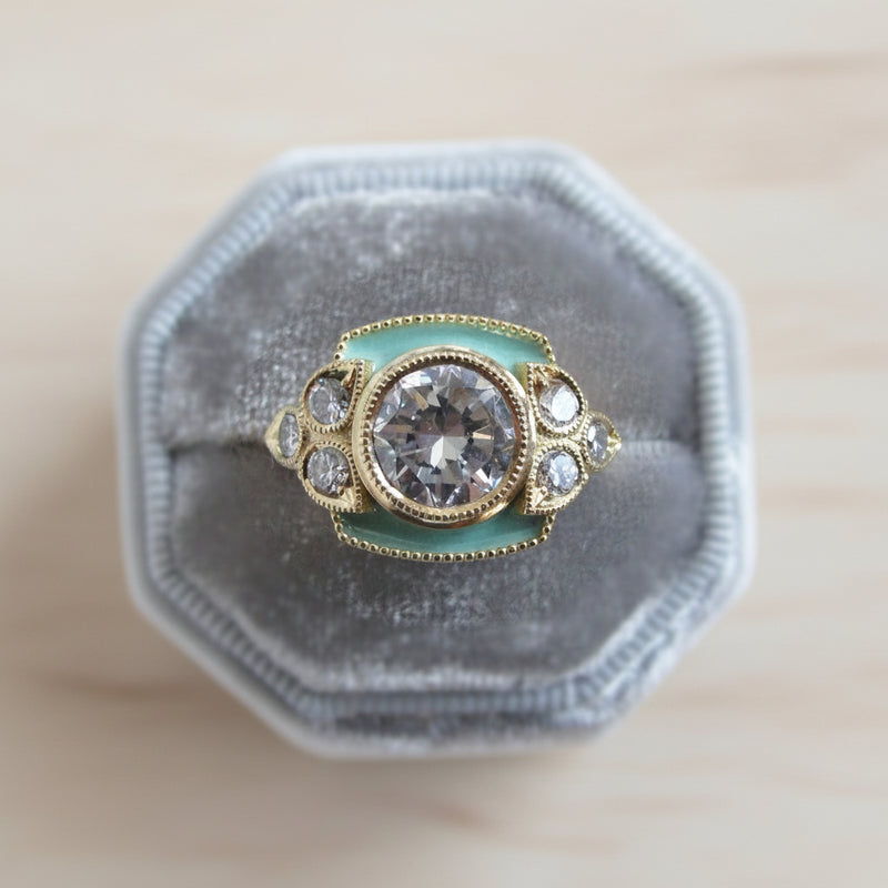 Gold and diamond ring on a gray velvet cushion with a plant in the background