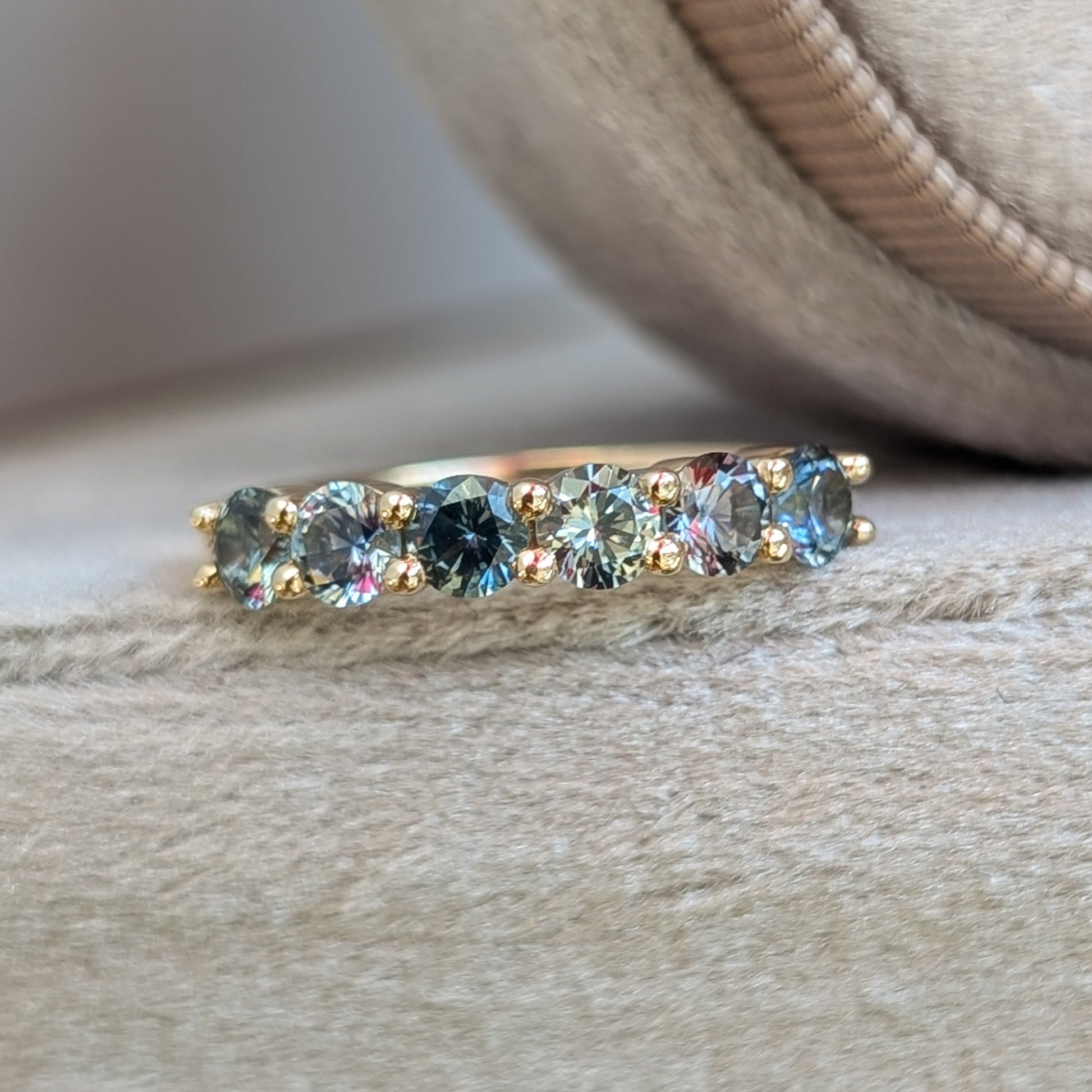 Gold ring with embedded teal gemstones on a velvet surface
