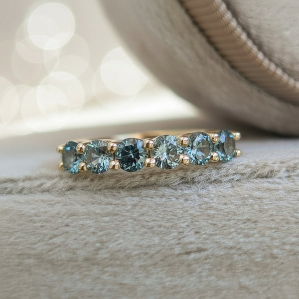 Gold ring with embedded teal gemstones on a velvet surface