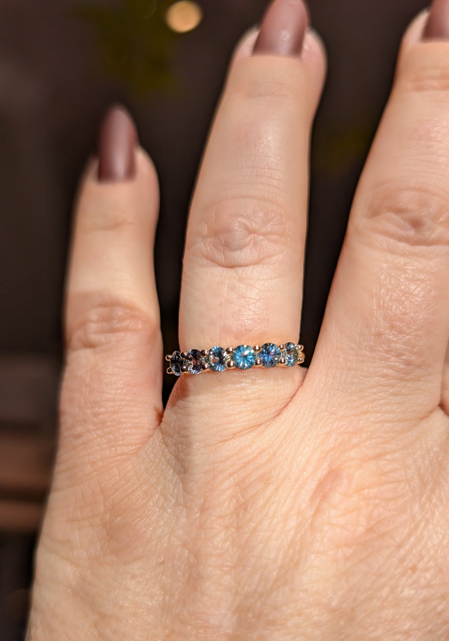 Close-up of a hand wearing a ring with blue gemstones on a blurred background
