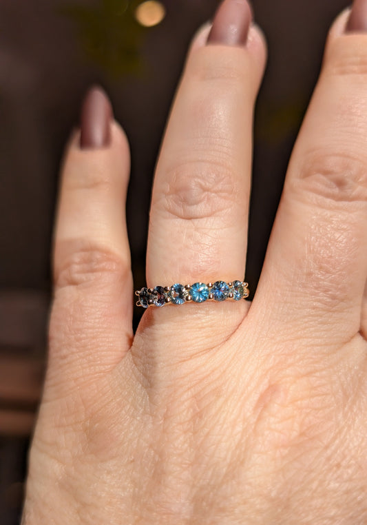Close-up of a hand wearing a ring with blue gemstones on a blurred background