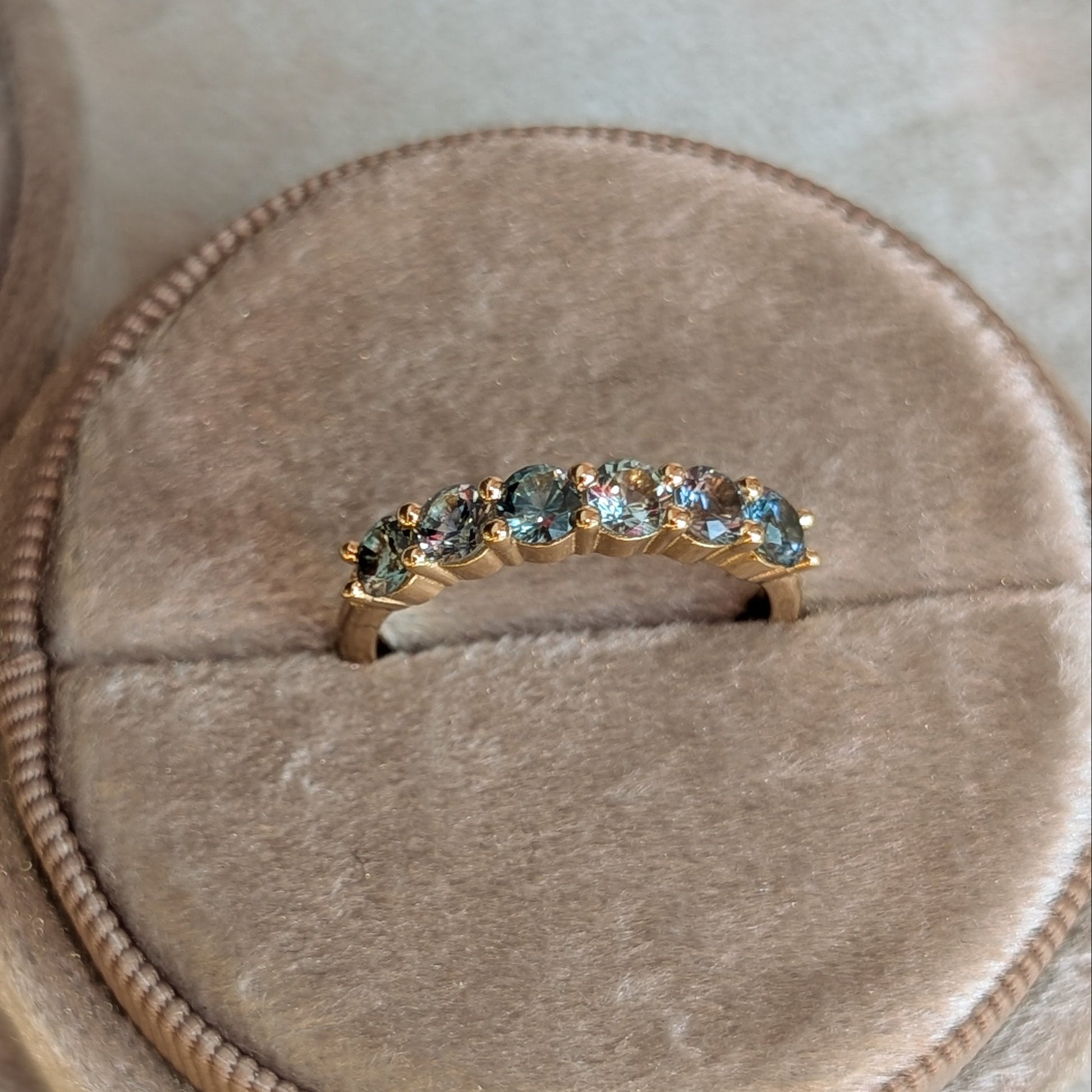 Gold ring with embedded stones on a beige velvet cushion