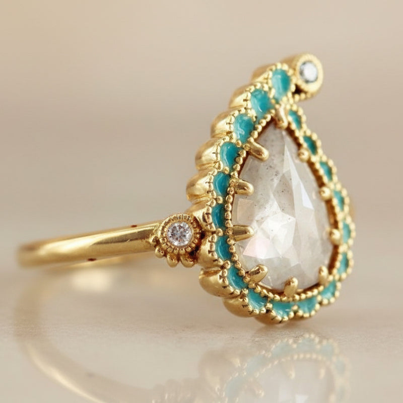 Gold ring with a paisley-shaped center stone and turquoise accents on a light background