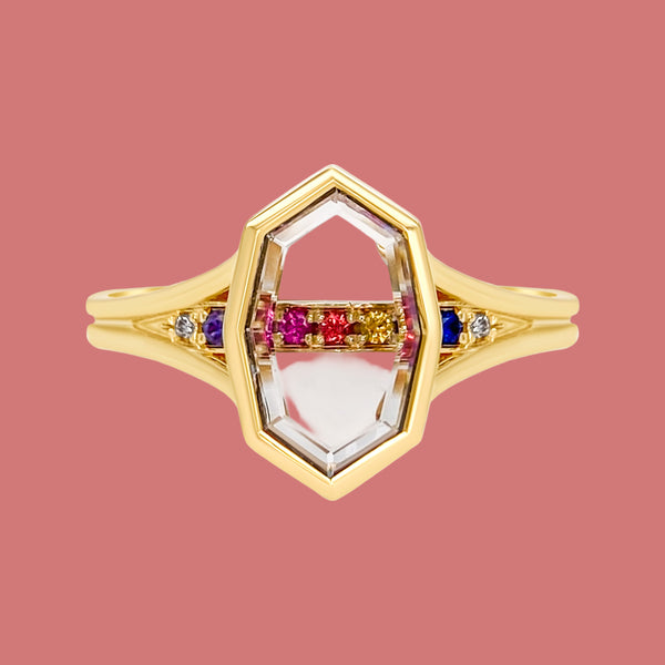 A split shank engagement ring with a white portrait cut sapphire centerpiece, surrounded by round mixed cut sapphires and FG VS round diamonds, all set in 14K yellow gold.