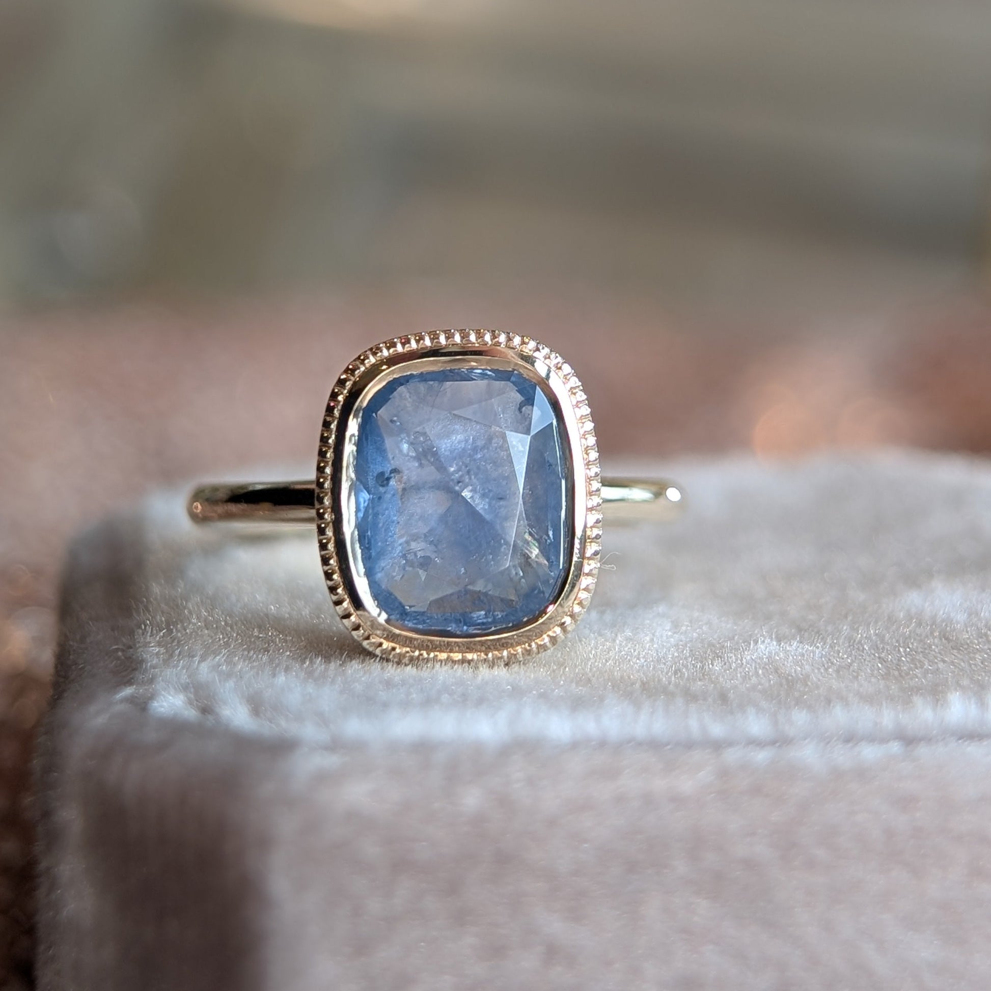 Ring with a blue gemstone and gold band on a soft surface