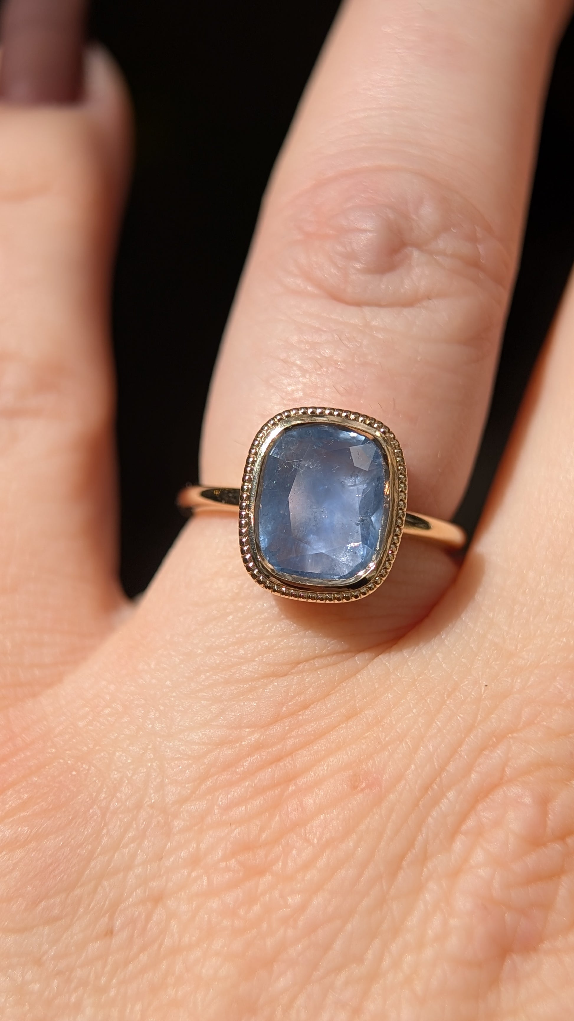 Blue gemstone ring on a finger with a dark background