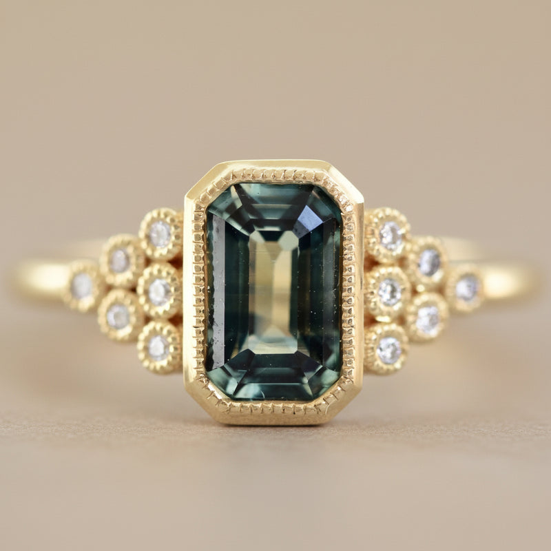 Gold ring with a green gemstone and diamond accents on a light background