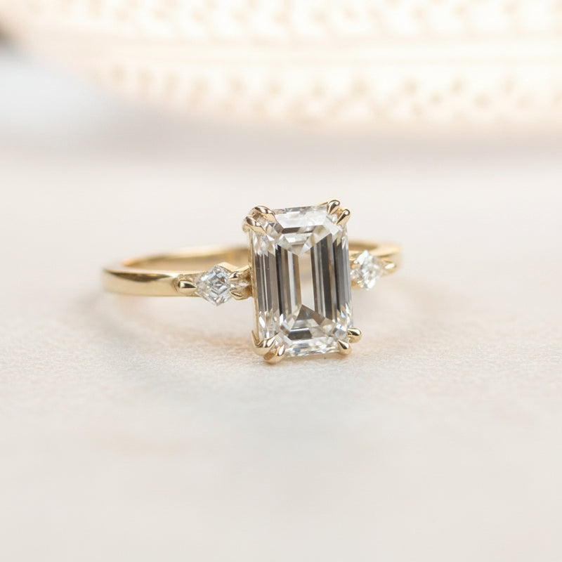 Gold ring with emerald-cut diamond on a white surface
