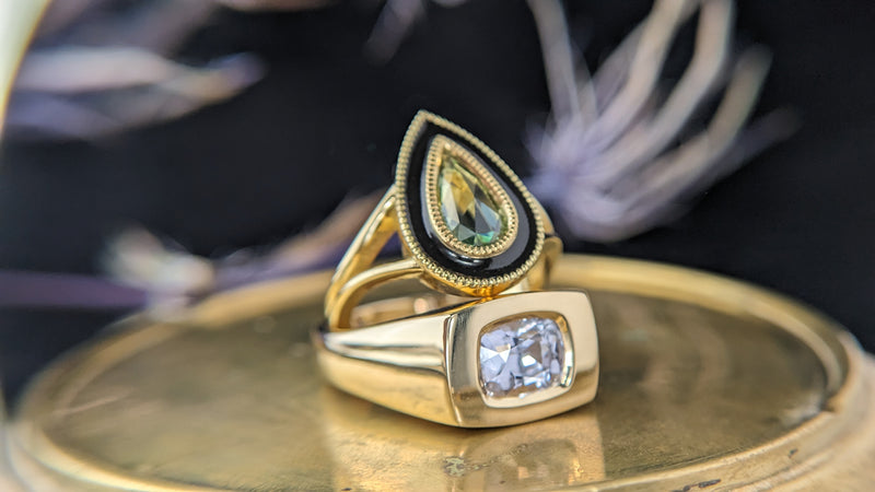 Two gold rings with gemstones on a reflective surface