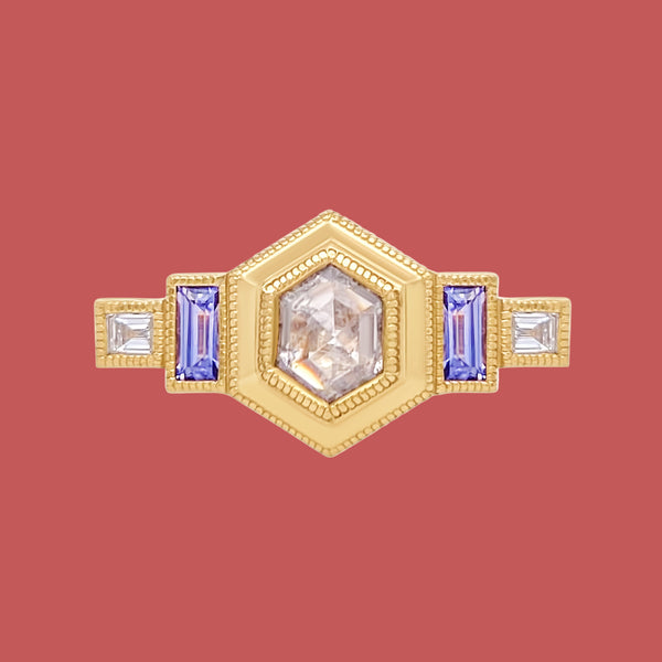 A 14k yellow gold ring featuring a hexagon rose cut natural diamond centerpiece with surrounding purple baguette sapphires and white baguette cut diamonds, set in a slim band with a cathedral setting.