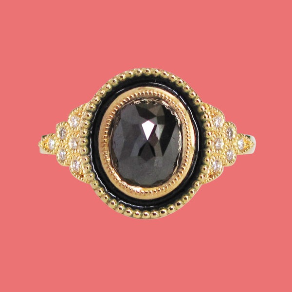 An 18K yellow gold engagement ring with a black diamond centerpiece and smaller clear diamond accents, featuring vitreous glass enamel inlay and miligrain accents.
