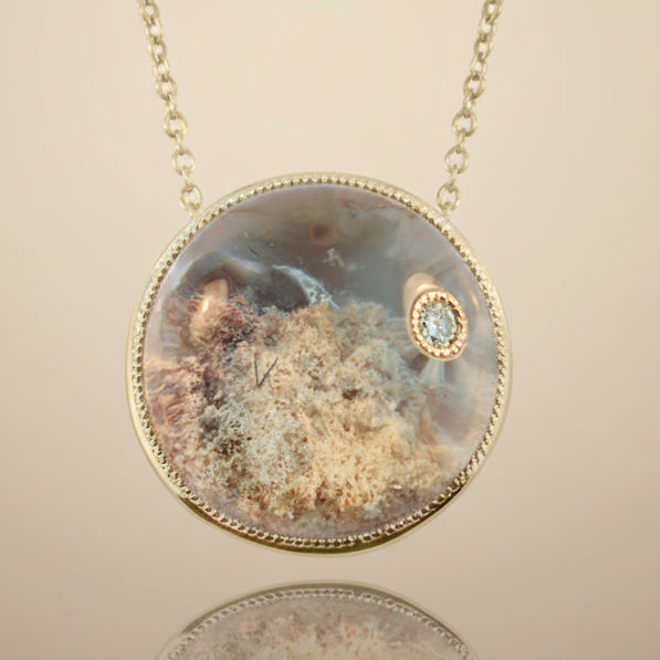 A round pendant necklace featuring a lodolite clear quartz crystal with gold-tone metal and a small diamond in the center.
