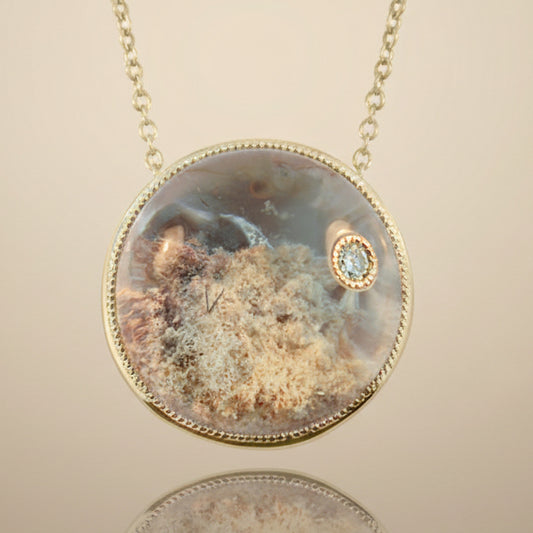 A round pendant necklace featuring a lodolite clear quartz crystal with gold-tone metal and a small diamond in the center.