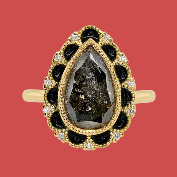 A pear-shaped diamond ring with vitreous enamel detailing in black, set in an 18k yellow gold band.